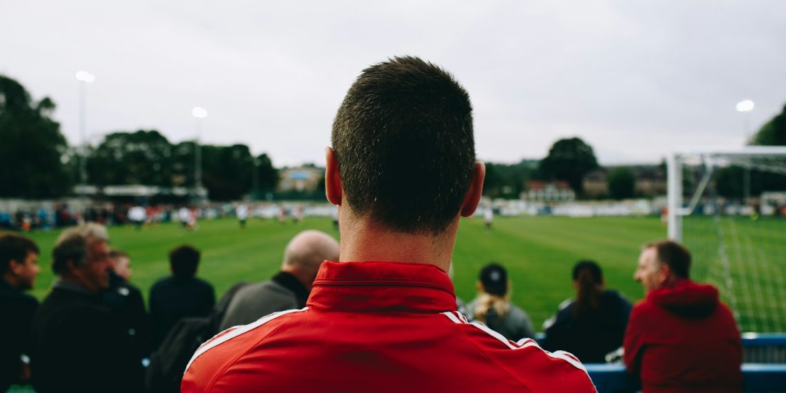 man standing while watching soccer during daytime