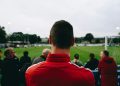 man standing while watching soccer during daytime