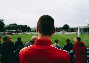 man standing while watching soccer during daytime